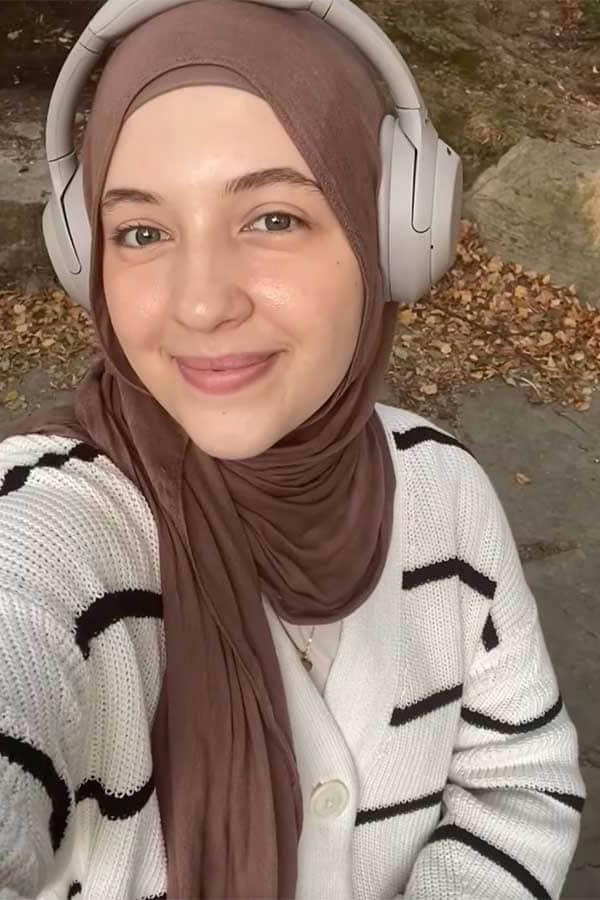 Nejla, a female 博彩网址大全 student, smiles for a selfie. She is wearing a brown hijab and white headphones.